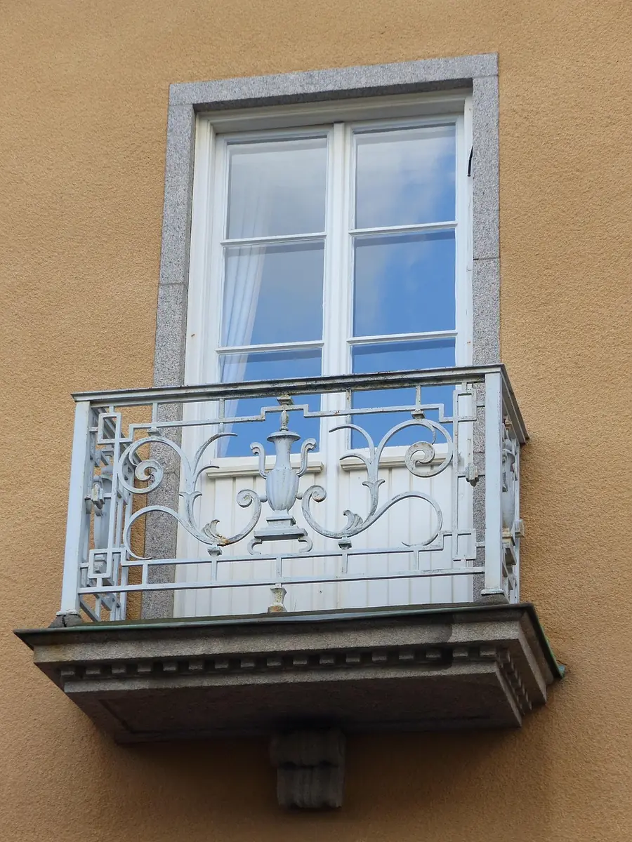 Balcon en fer forgé blanc vu de face : garde-corps à volutes posé sur la dalle, devant une porte-fenêtre
