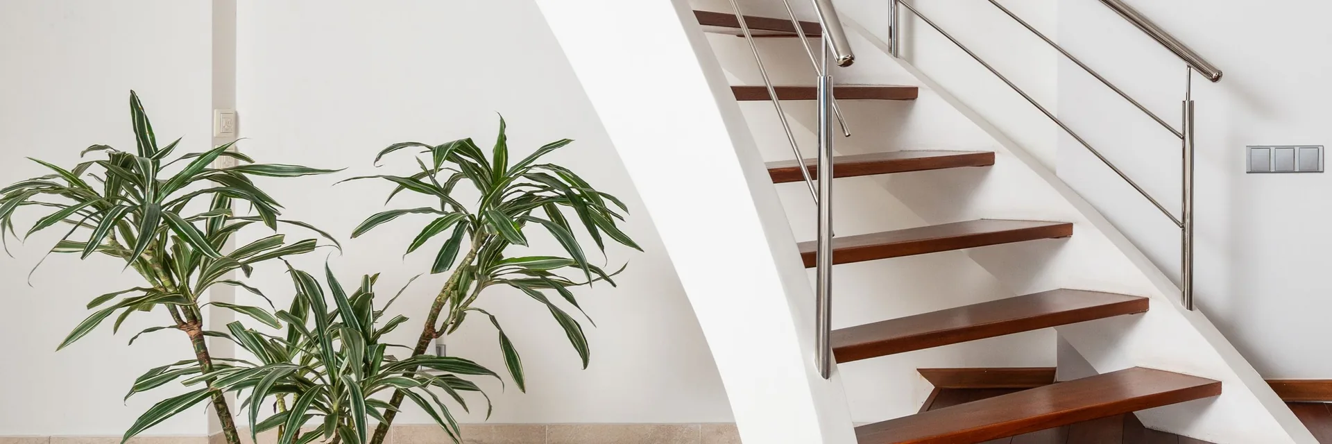 Escalier courbe blanc à marches en bois, avec sa rampe en inox