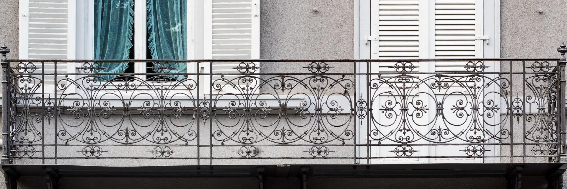 Garde-corps de balcon en fer forgé à volutes devant des volets blancs