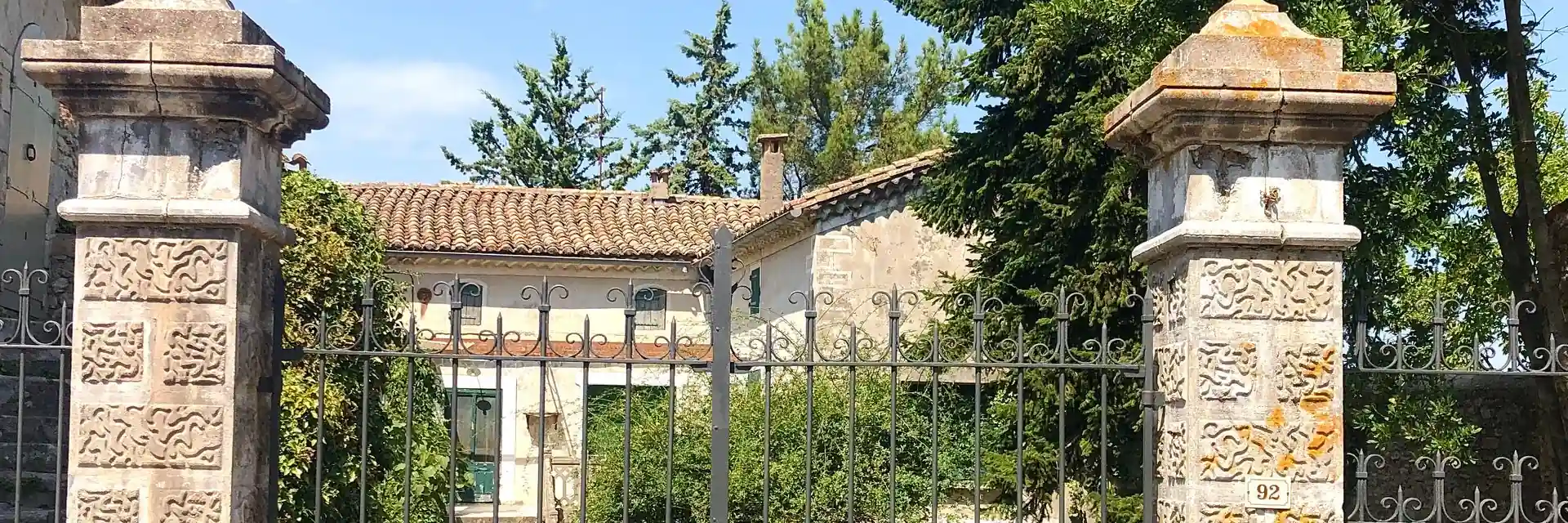 Portail métallique entre deux piliers de pierre devant une maison à toit de tuiles