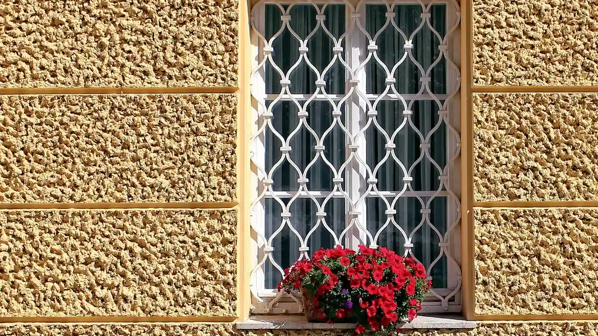 Grille de défense en fer à losanges devant une fenêtre fleurie