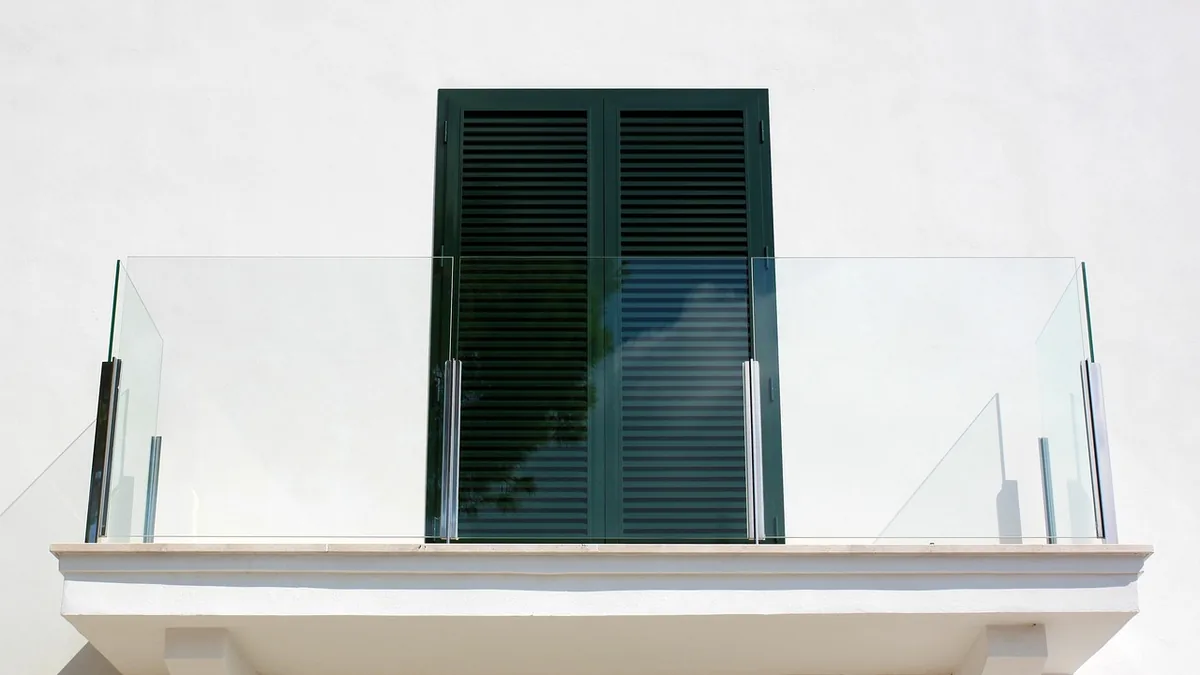 Garde-corps de balcon en verre sur poteaux inox, devant une porte-fenêtre à volets