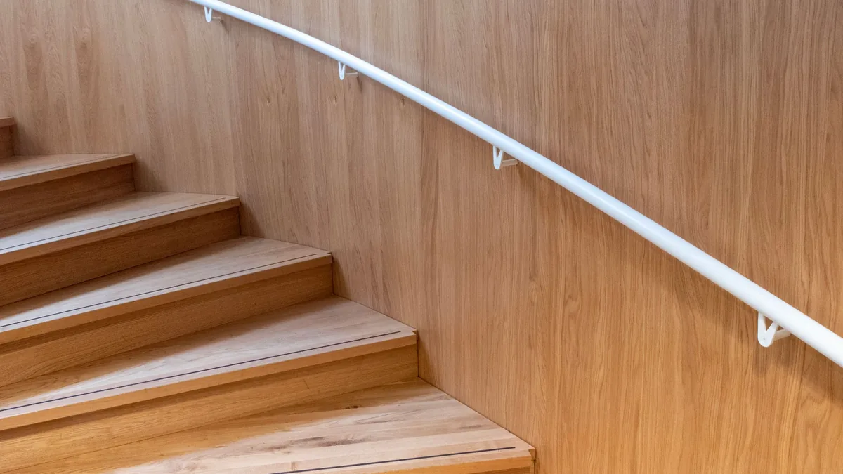 Main courante métallique blanche fixée au mur d'un escalier lambrissé de bois