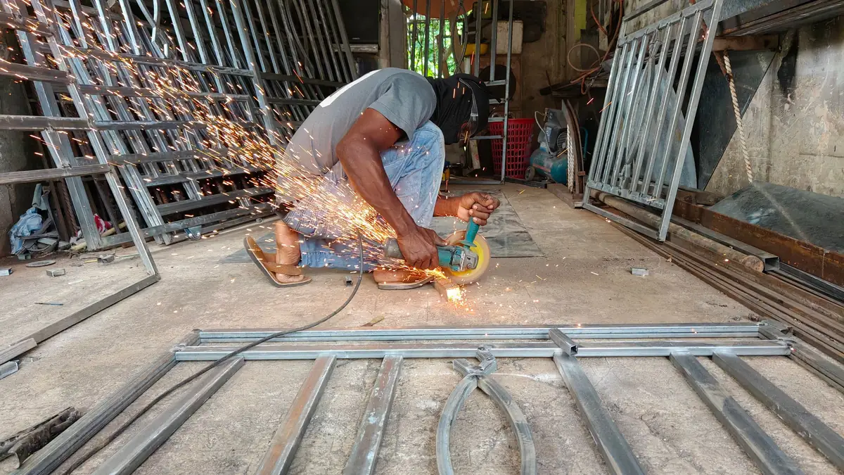 Atelier de fabrication : un ouvrier meule des vantaux de portail