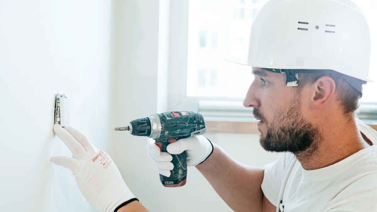 Ouvrier qui perce un mur à la visseuse pour fixer une rampe