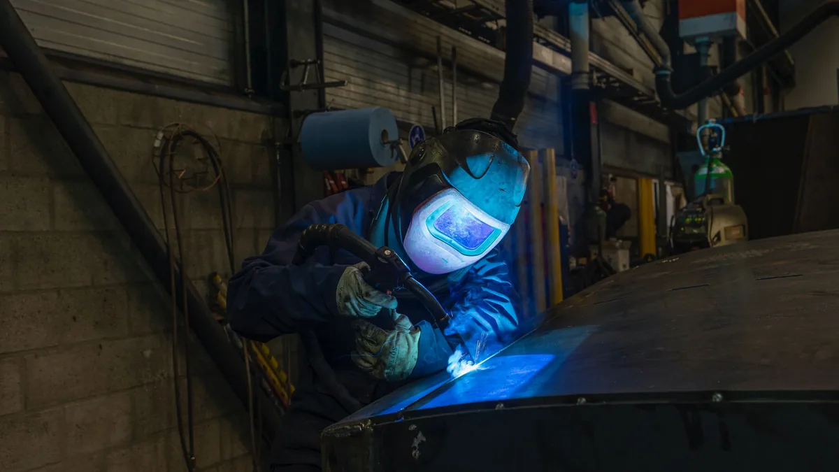 Soudeur masqué penché sur sa pièce dans un atelier, lueur bleue de l'arc
